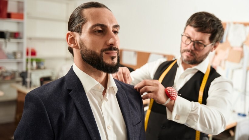 Seamstress vs tailor - A tailor taking measurements for a suit sleeve.