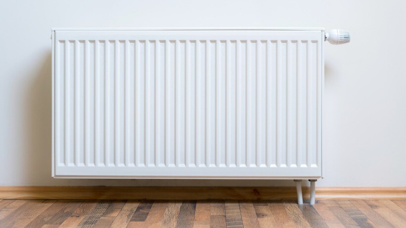 Underfloor heating vs radiators - Home radiator heater on the white wall on wooden hardwood floor