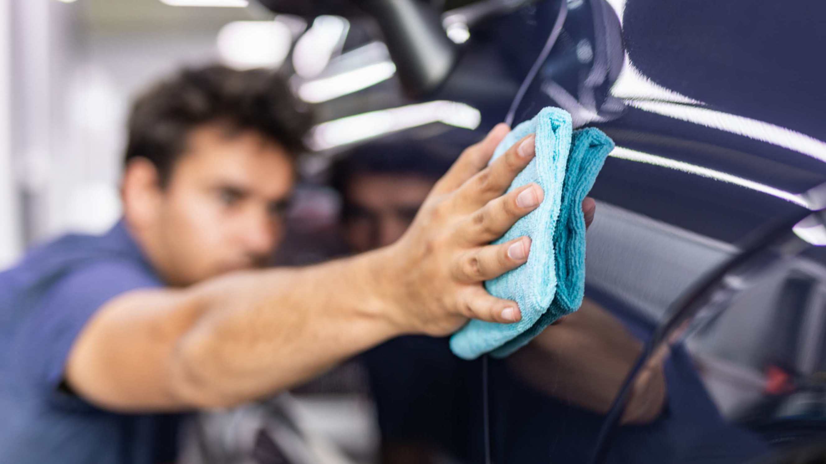 Car polish vs. wax - A person using a blue microfiber cloth to polish or wax a car.