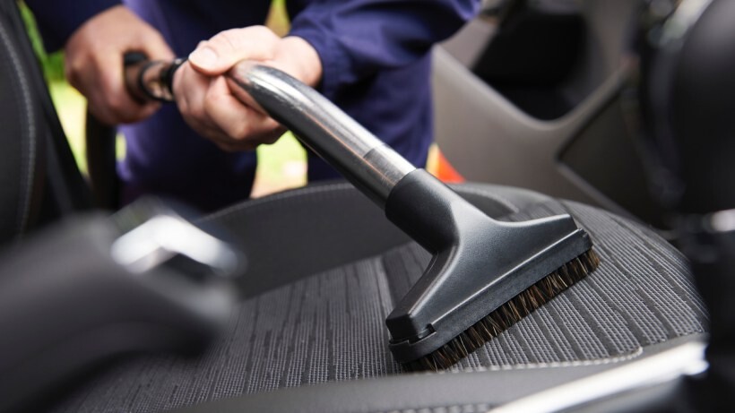 Car detailing vs car wash - A person using a vacuum cleaner attachment to clean the interior of a car