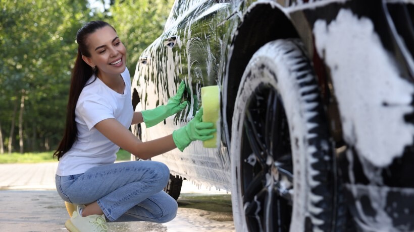 Car detailing vs car wash - A person washing a car with a sponge and bucket