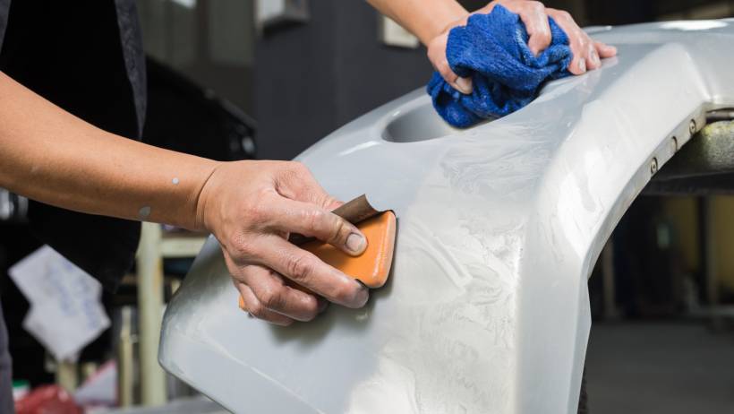 A mechanic sanding a car bumper in preparation for painting. - car respray cost