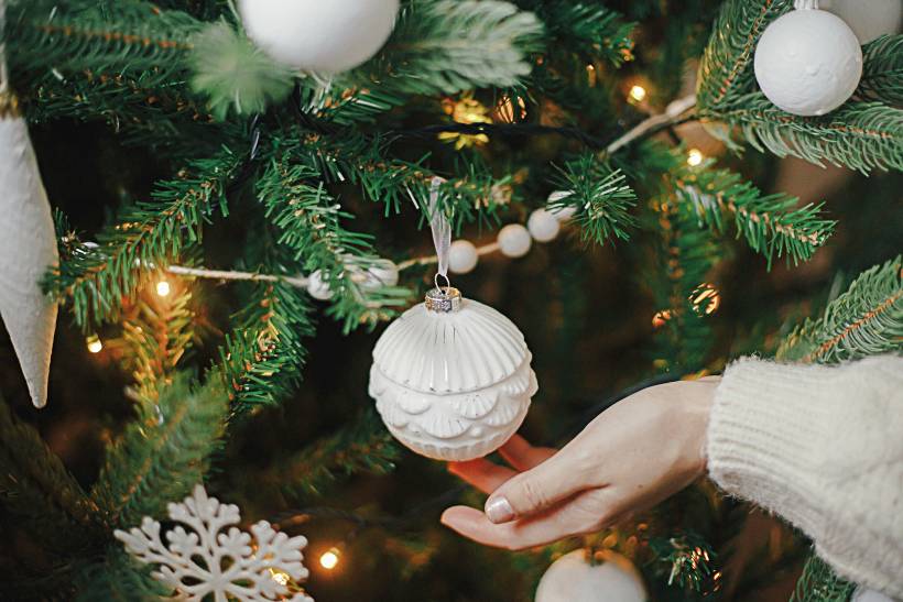 getting ready for the holidays - a woman decorating a stylish boho Christmas tree with vintage ornaments