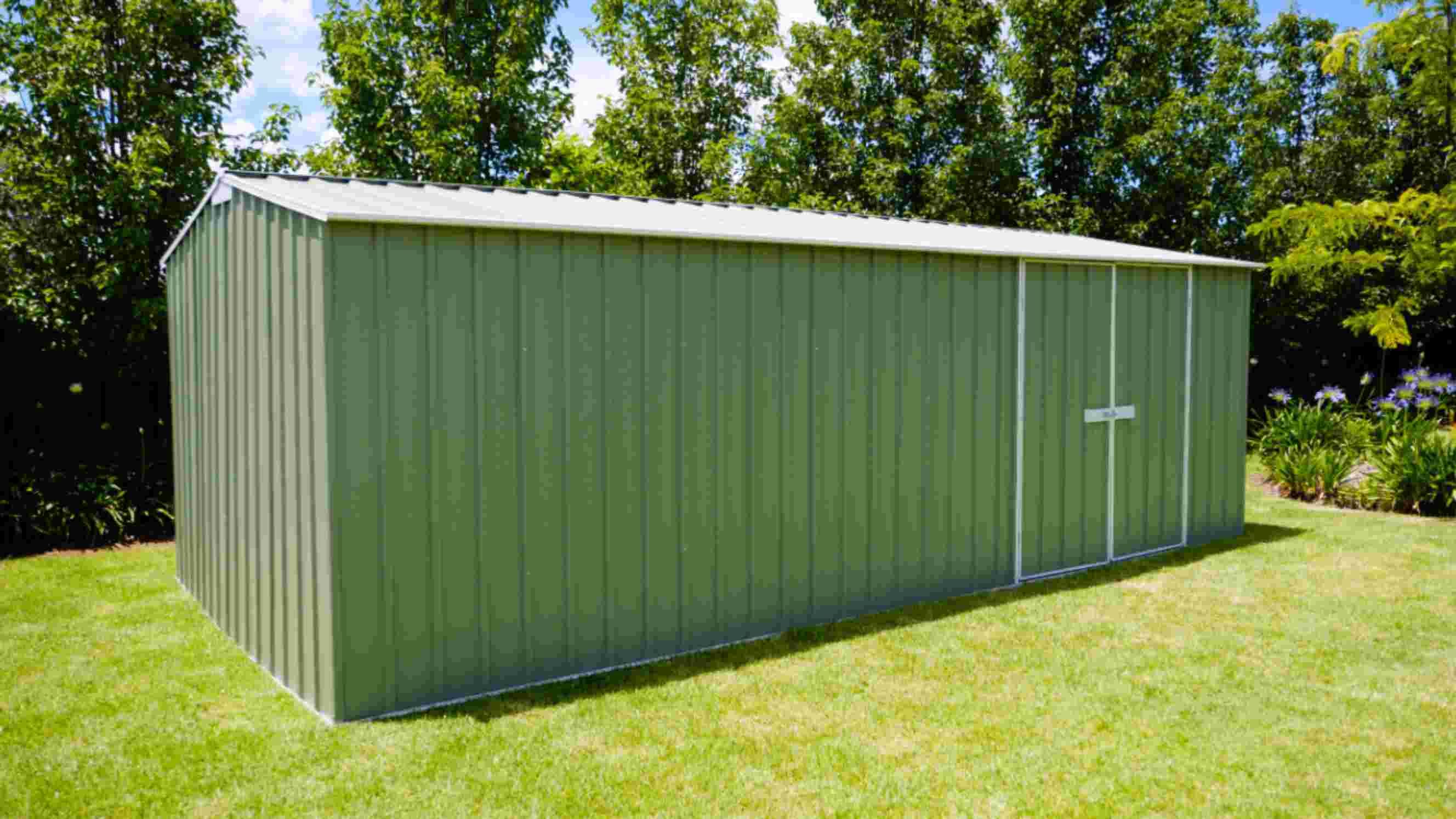 Green workshop shed installed in a lush garden surrounded by trees and greenery.