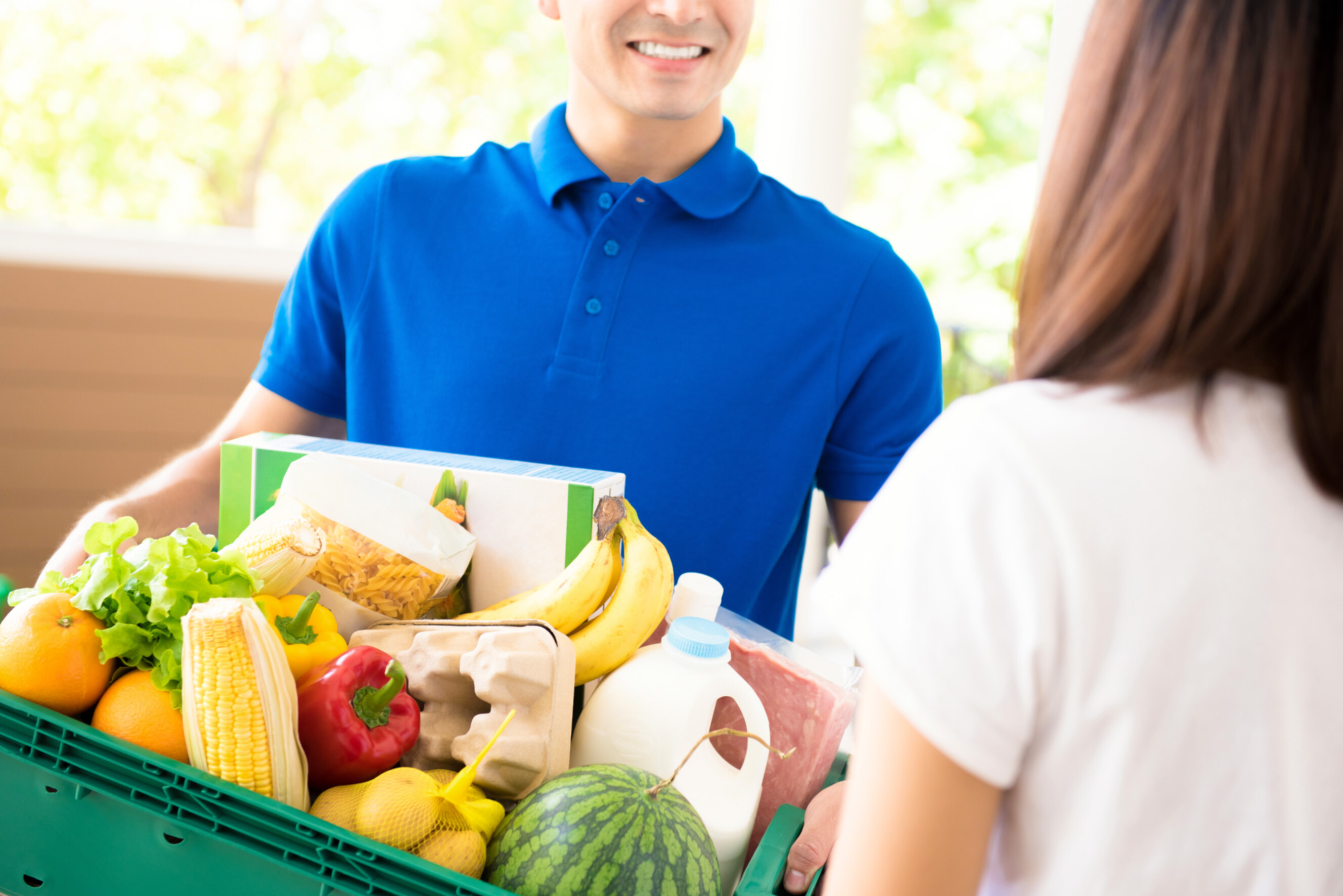 Smiling grocery delivery expert handing a basket of fresh produce and essentials to a customer, showcasing reliable grocery delivery services near you.