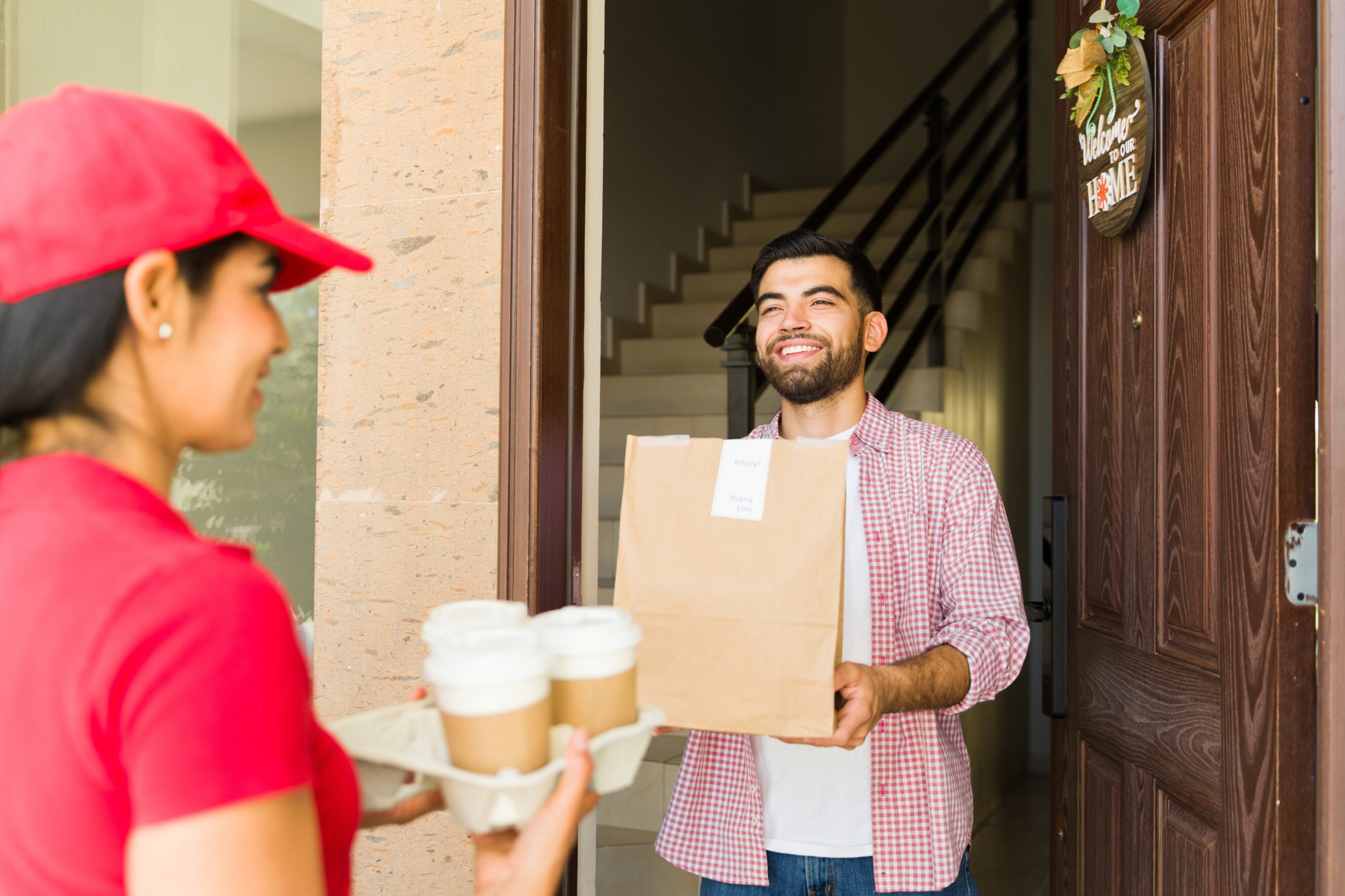 Smiling customer receiving coffee and a paper bag of food from a delivery professional, highlighting coffee pickup and delivery services near you.