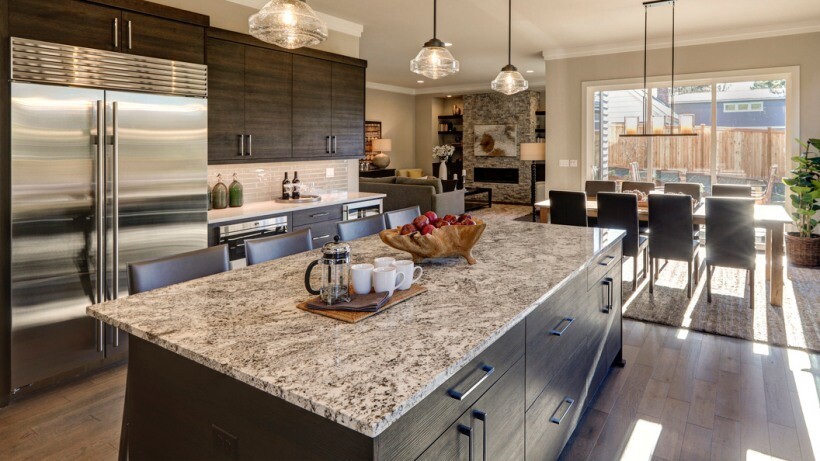 Quartz vs granite countertops - A luxurious kitchen featuring a large granite countertop with natural speckled patterns, dark wood cabinetry, and a spacious dining area with ample natural light