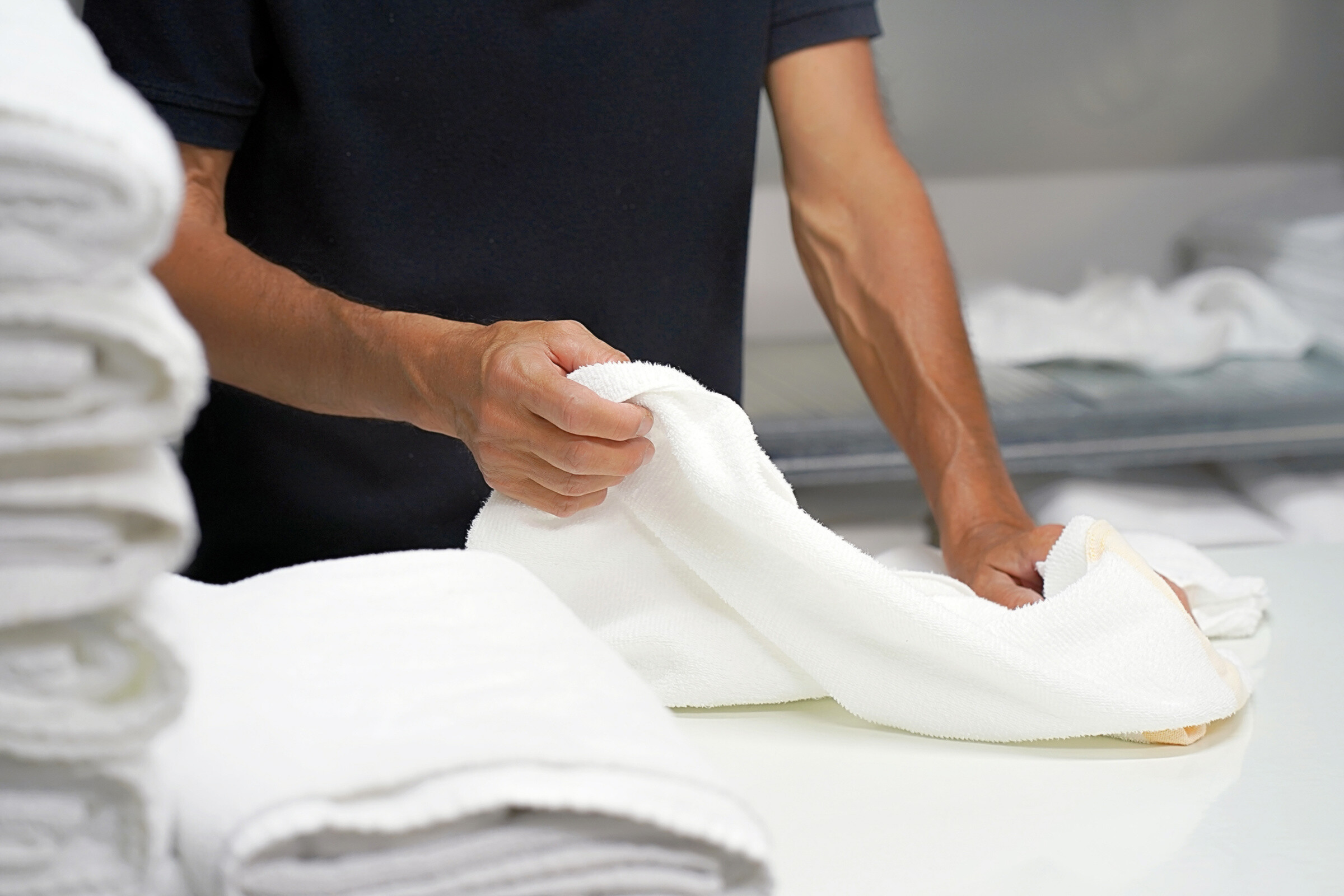 Hands of caucasian male laundry worker folds a clean white towel. 