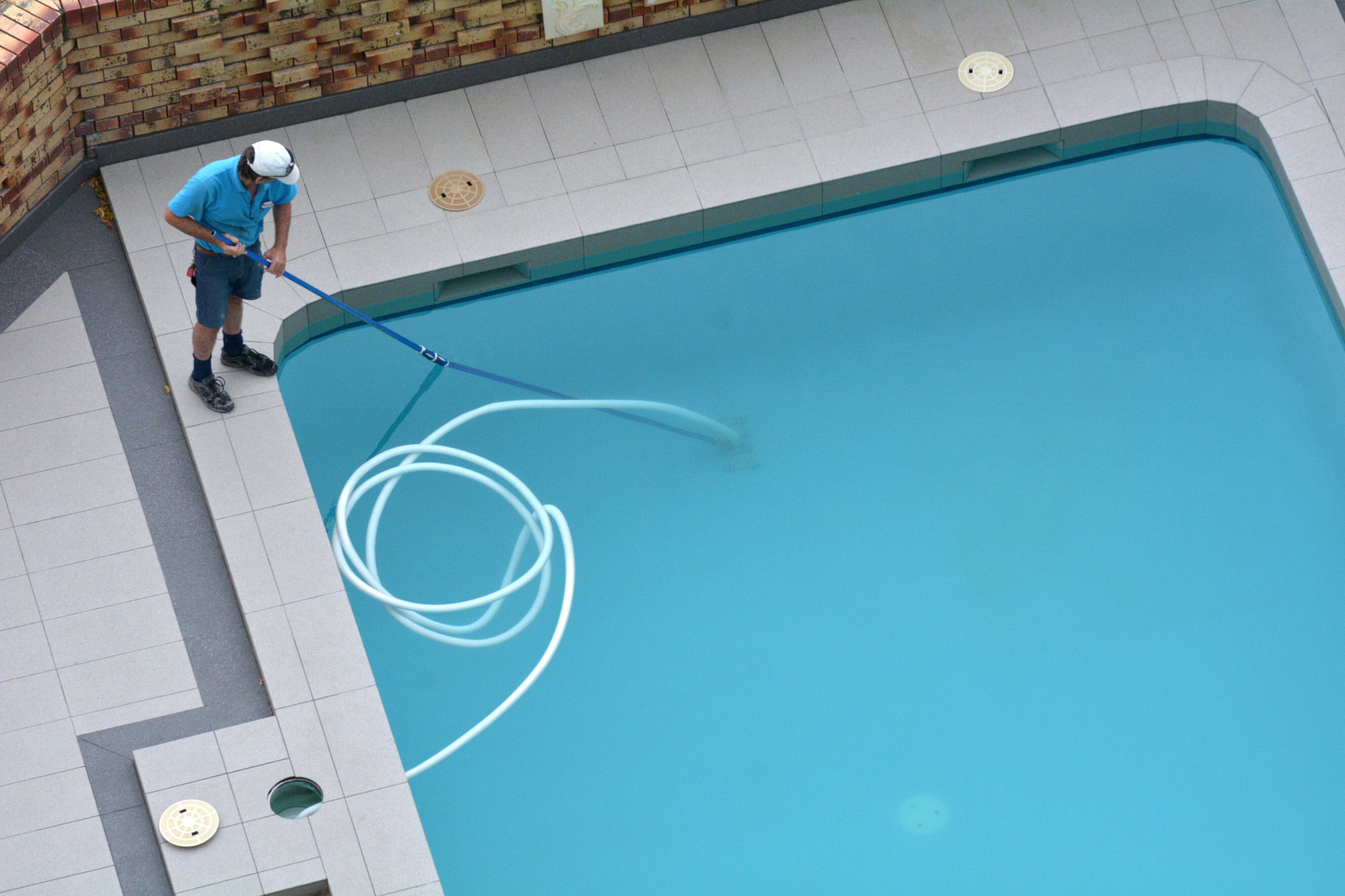 Professional pool cleaner using equipment to clean a residential swimming pool, highlighting expert pool cleaning services near you.