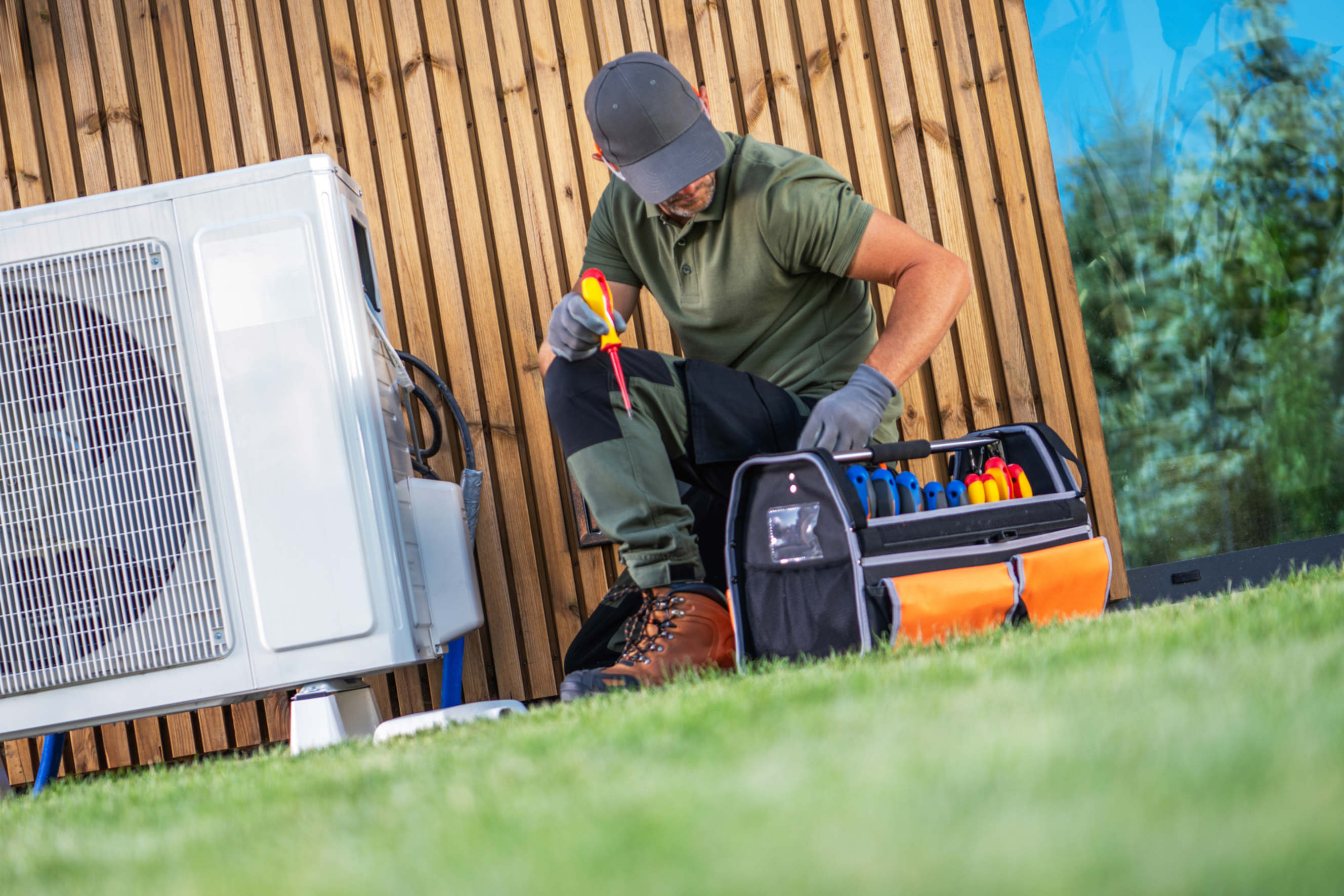 HVAC technician servicing a heat pump with a toolbox outdoors.