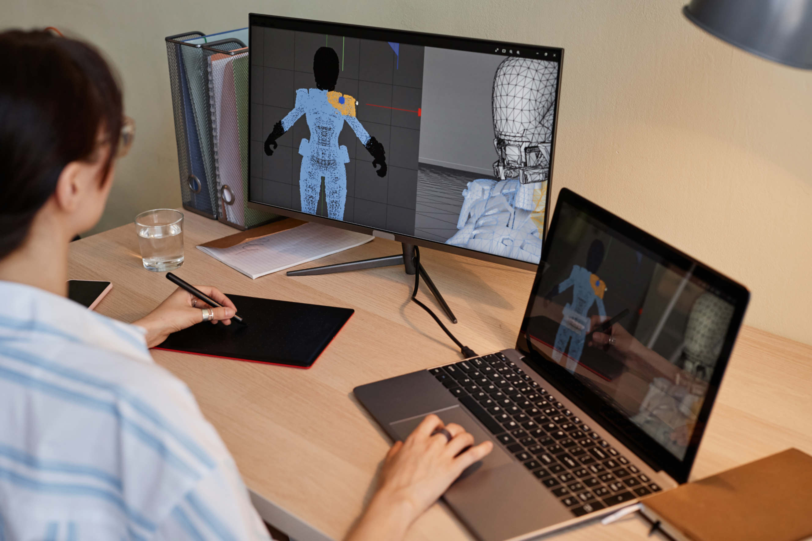 3D artist creating a digital character model using a drawing tablet and dual monitors.