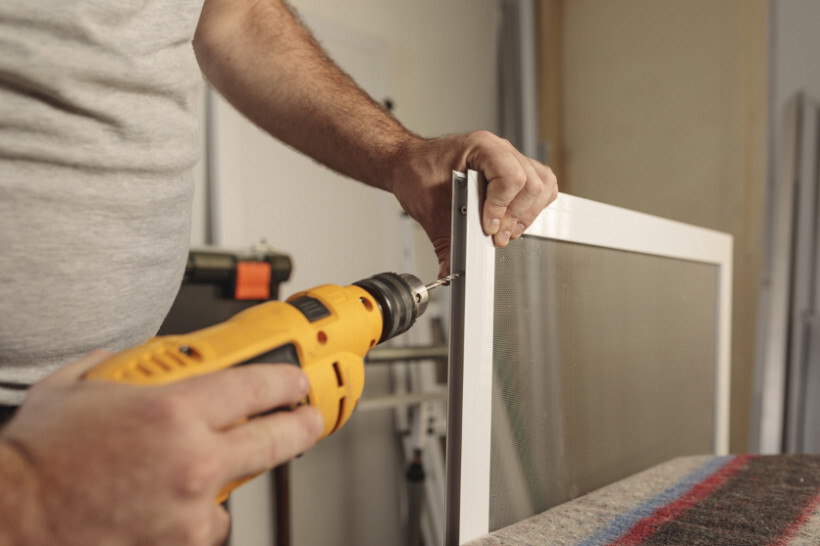 window screen installation - Worker using an electric drill to secure a window screen frame.