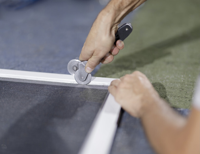 window screen installation - Using a spline roller tool to secure mesh in a window screen frame.