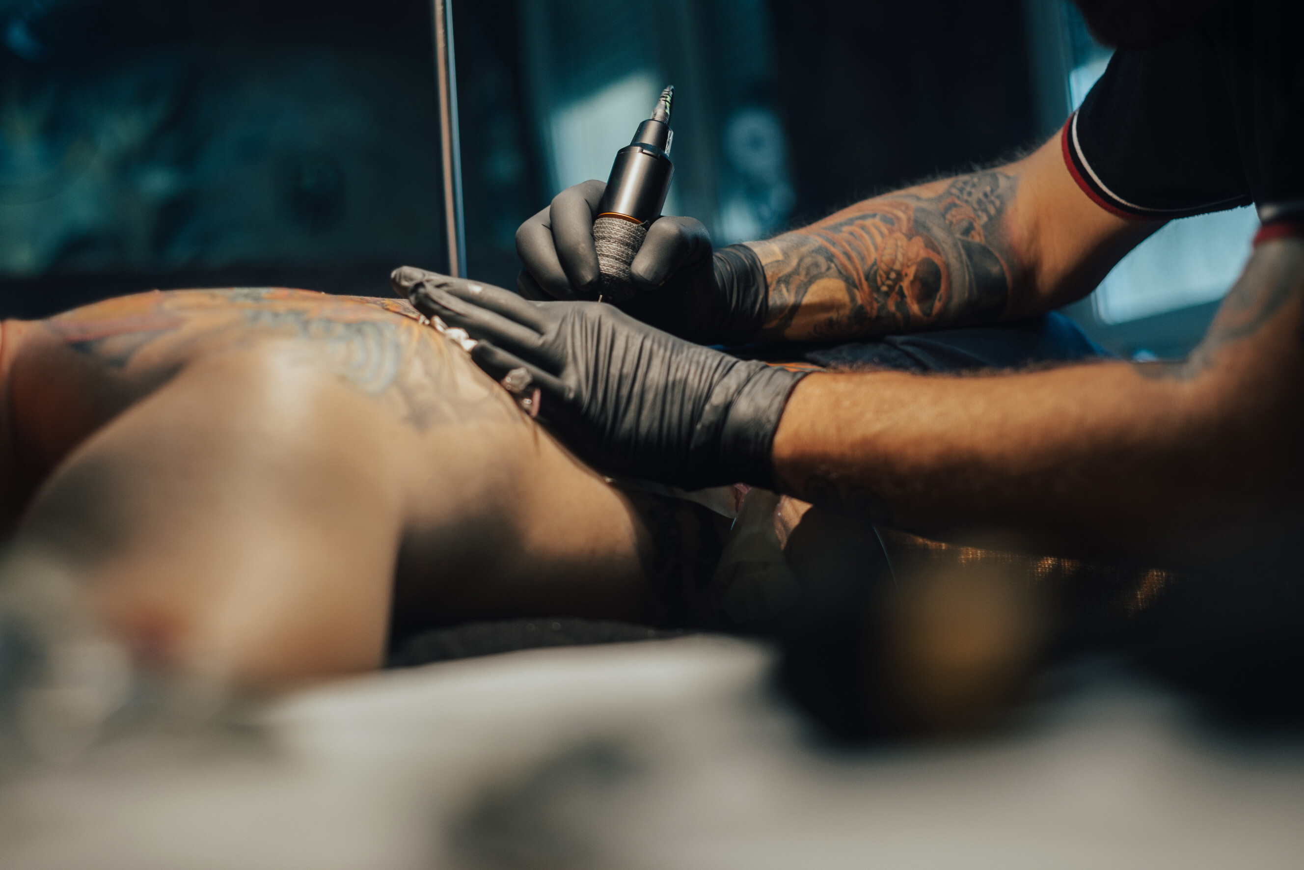 how much do tattoos cost - Tattoo artist applying a large, intricate back tattoo on a male client in a professional tattoo studio