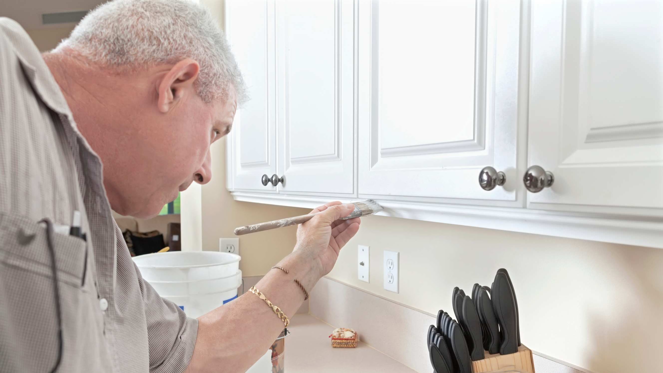 A person carefully painting white kitchen cabinets, representing kitchen cabinet painting