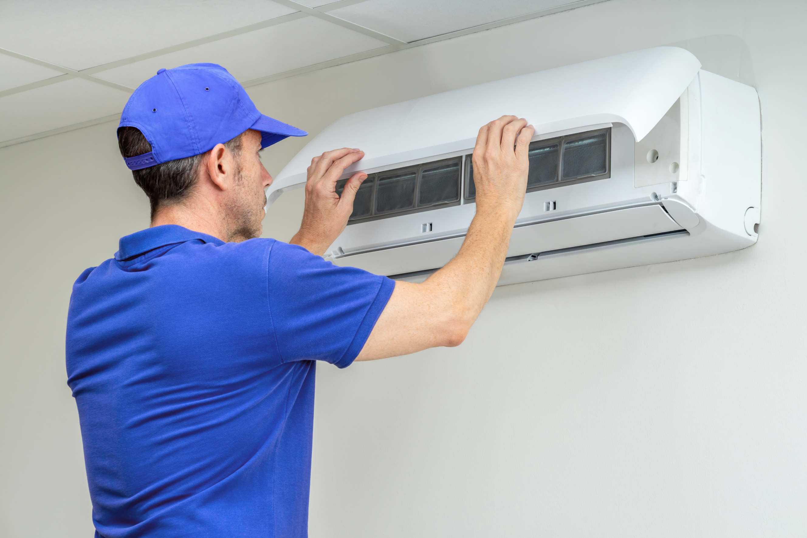 Technician in blue uniform servicing a wall-mounted air conditioner.