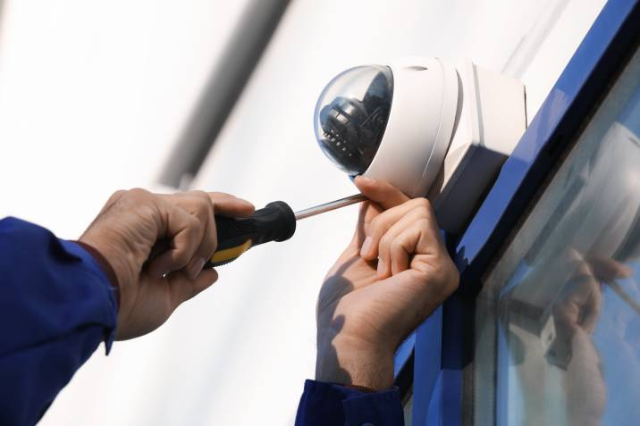 electrical side jobs - Close-up of an electrician installing a dome CCTV camera on a building exterior