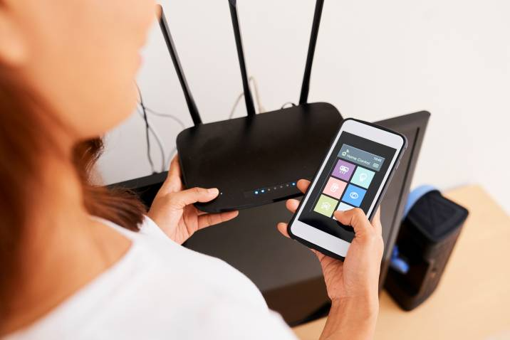 electrical side jobs - A woman configuring a home automation system using a smartphone and Wi-Fi router