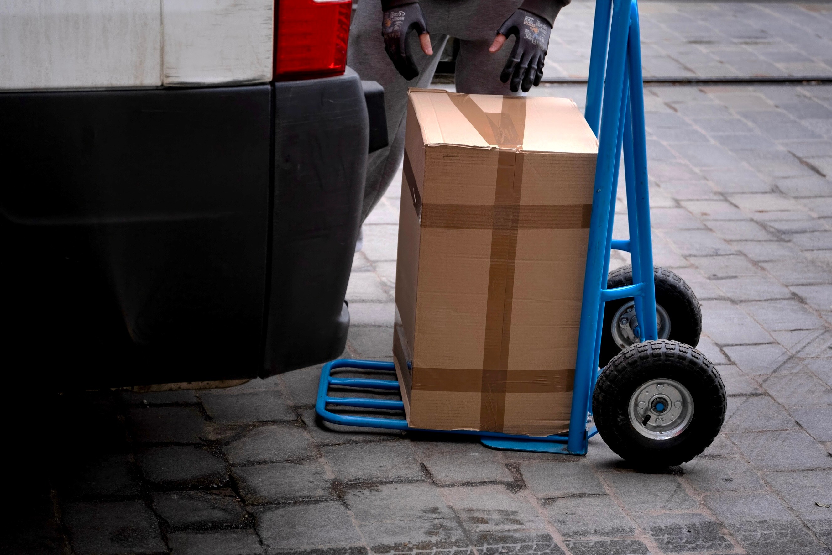Large cardboard box on a blue hand truck next to a moving van.