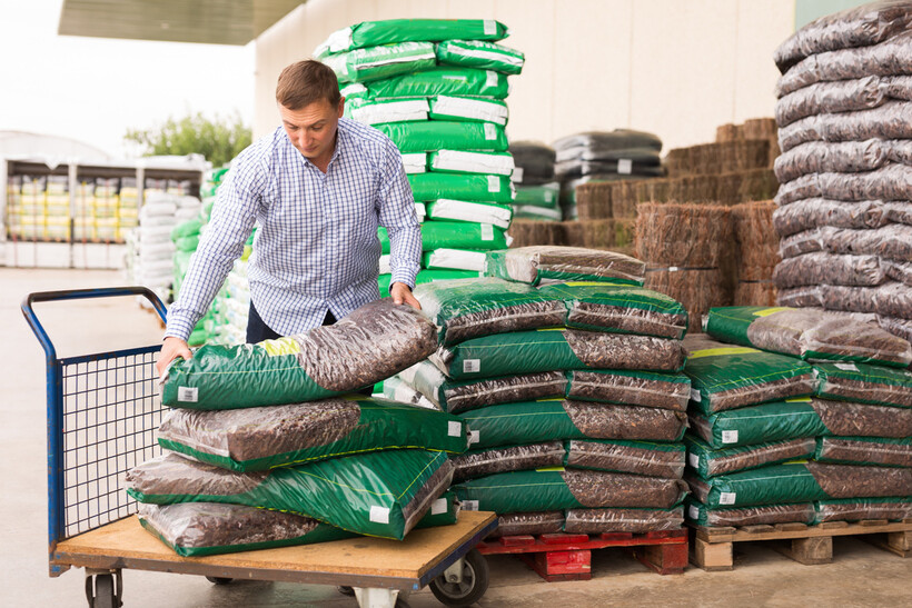 Man stacking bags of soil or mulch on a cart in a garden supply store. - compost vs fertilizer