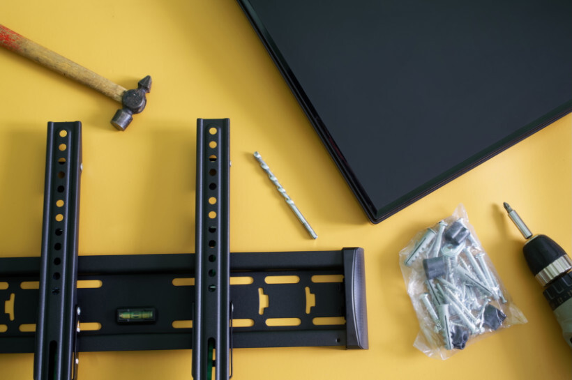 how to wall mount tv – Wall mount bracket, drill, screws, and tools laid out next to a flat-screen TV.