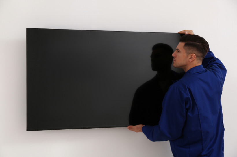 how to wall mount tv – Technician carefully positioning a flat-screen TV onto a wall bracket.
