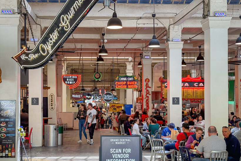 Neon signs glowing above busy food stalls in a crowded indoor market. - moving to Los Angeles