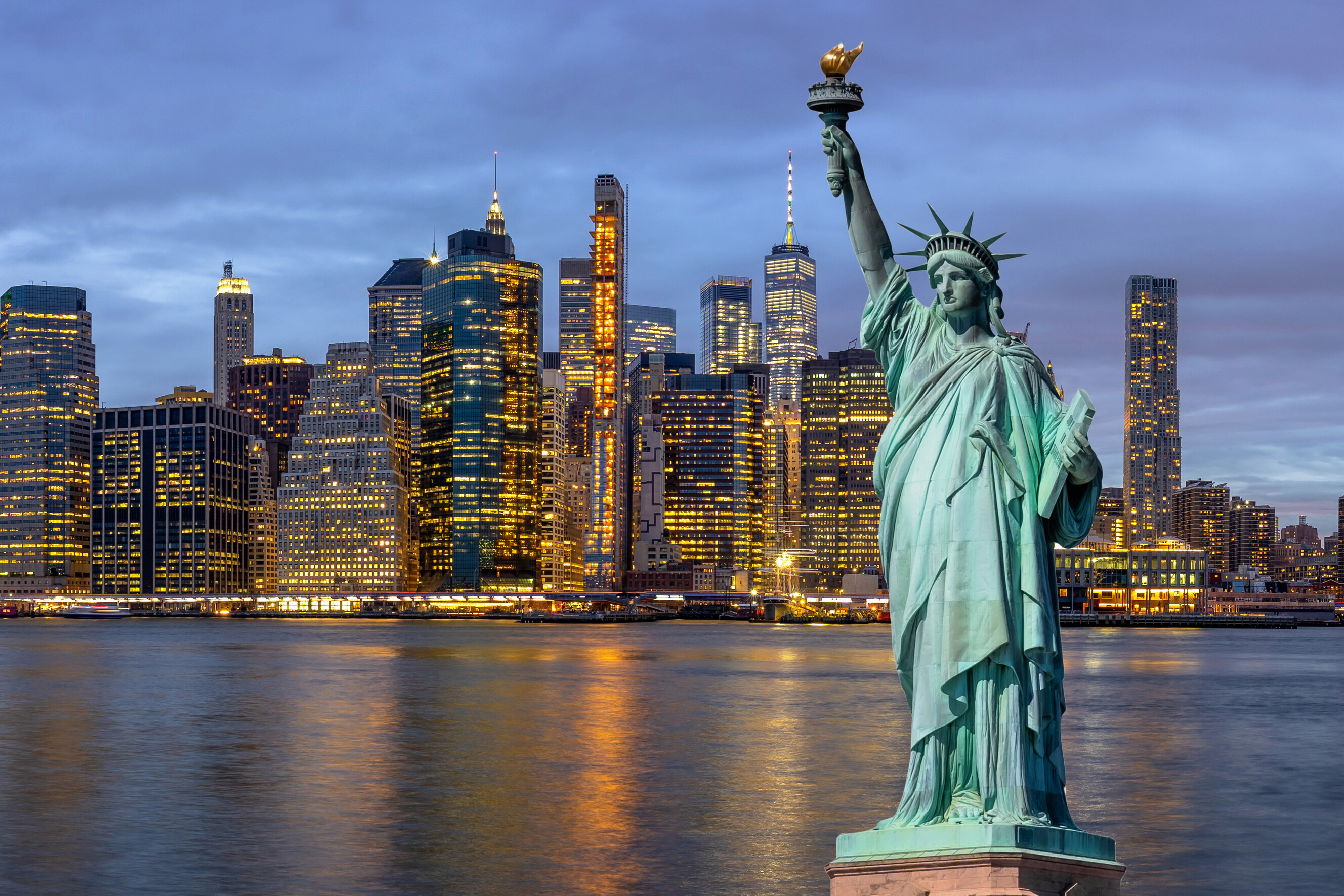 A panoramic shot of the iconic Statue of Liberty overlooking the city harbor and bridges.