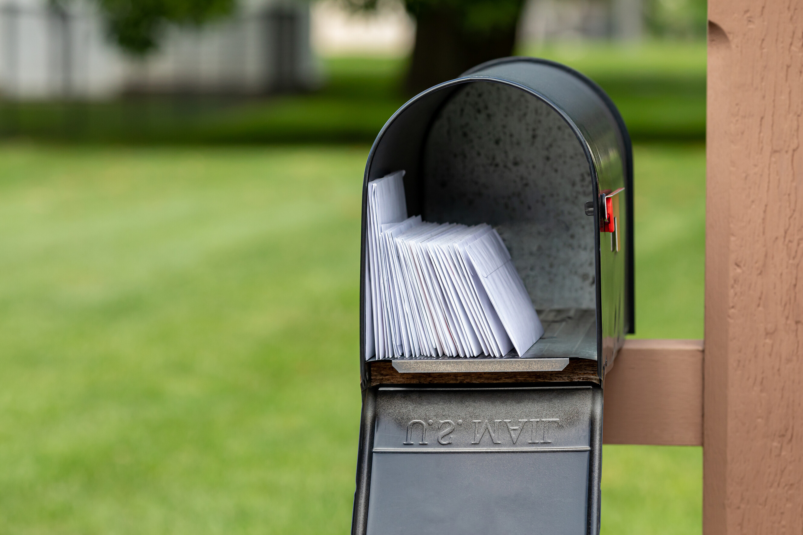 A black curbside mailbox stuffed with various white envelopes.