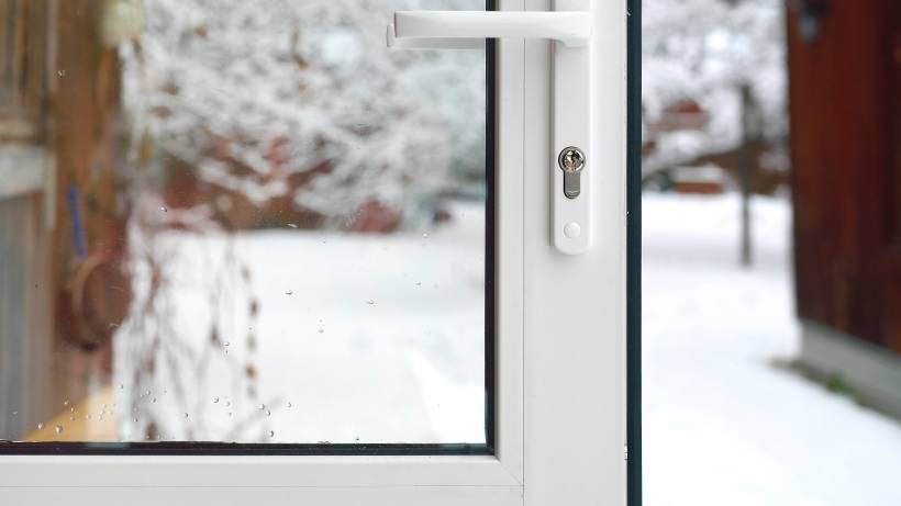 Close-up of a white storm door frame and glass pane covered in condensation with snow-covered trees in the background. - cost to install a storm door