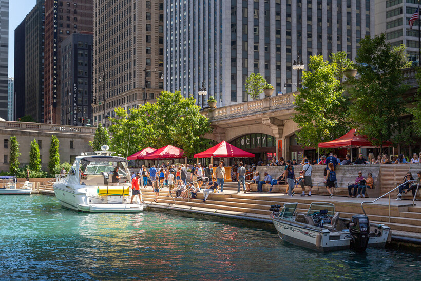 A sunny day view of pedestrians enjoying the waterfront walkway along the Chicago River. - moving to Chicago
