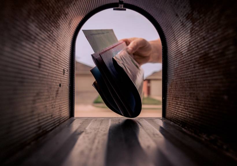 mailbox installation cost - Mail delivery with a hand inserting envelopes into a mailbox in a neighborhood setting