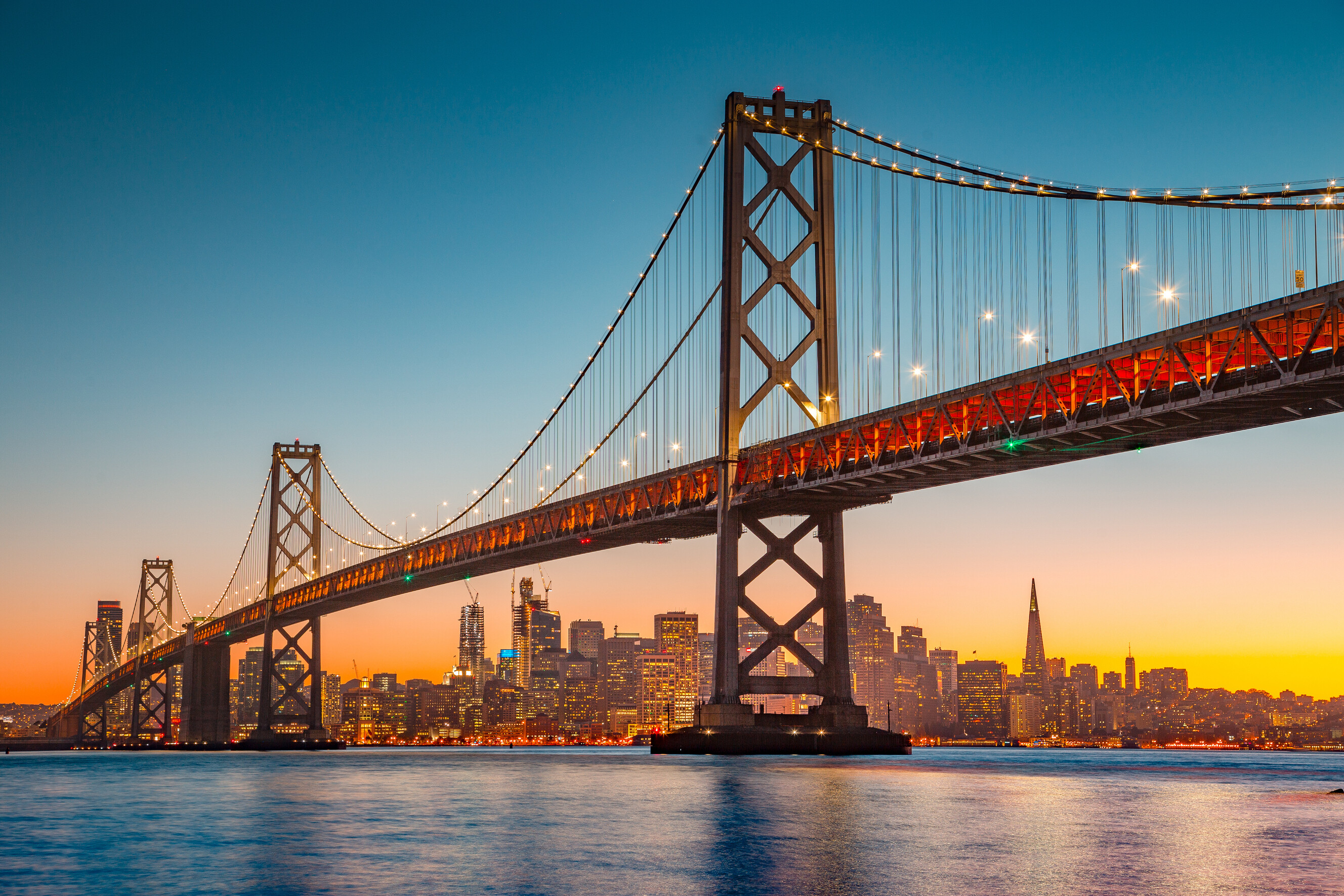 A panoramic sunset view of the San Francisco city skyline and the Oakland Bay Bridge.