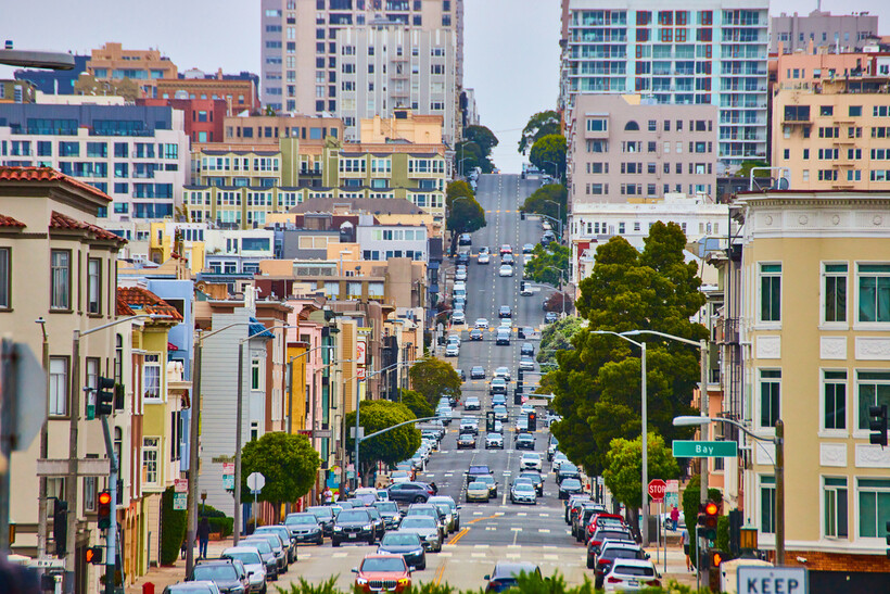 Cars parked on a very steep residential hill with city buildings in the background. - moving to San Francisco