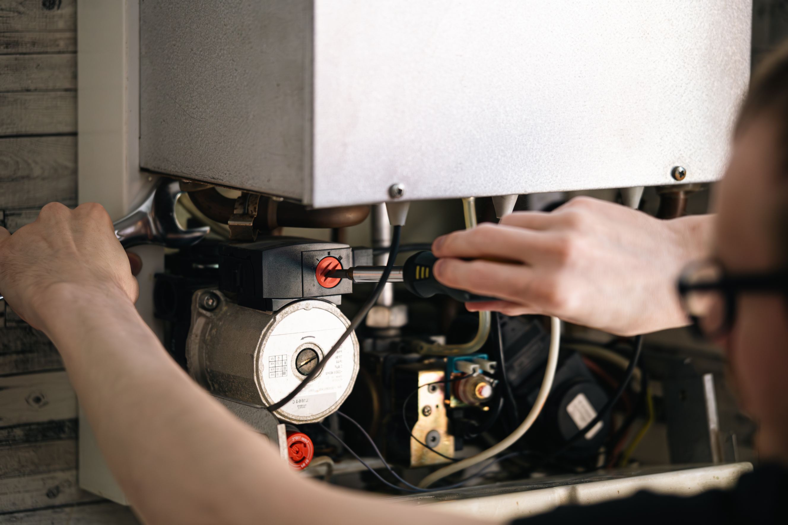 Man is repairing a heating boiler, a screwdriver and a spanner in his hands, representing heater maintenance near me.