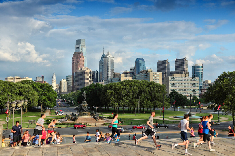 Runners on the steps of the Philadelphia Museum of Art with skyline views behind them. - moving to Philadelphia