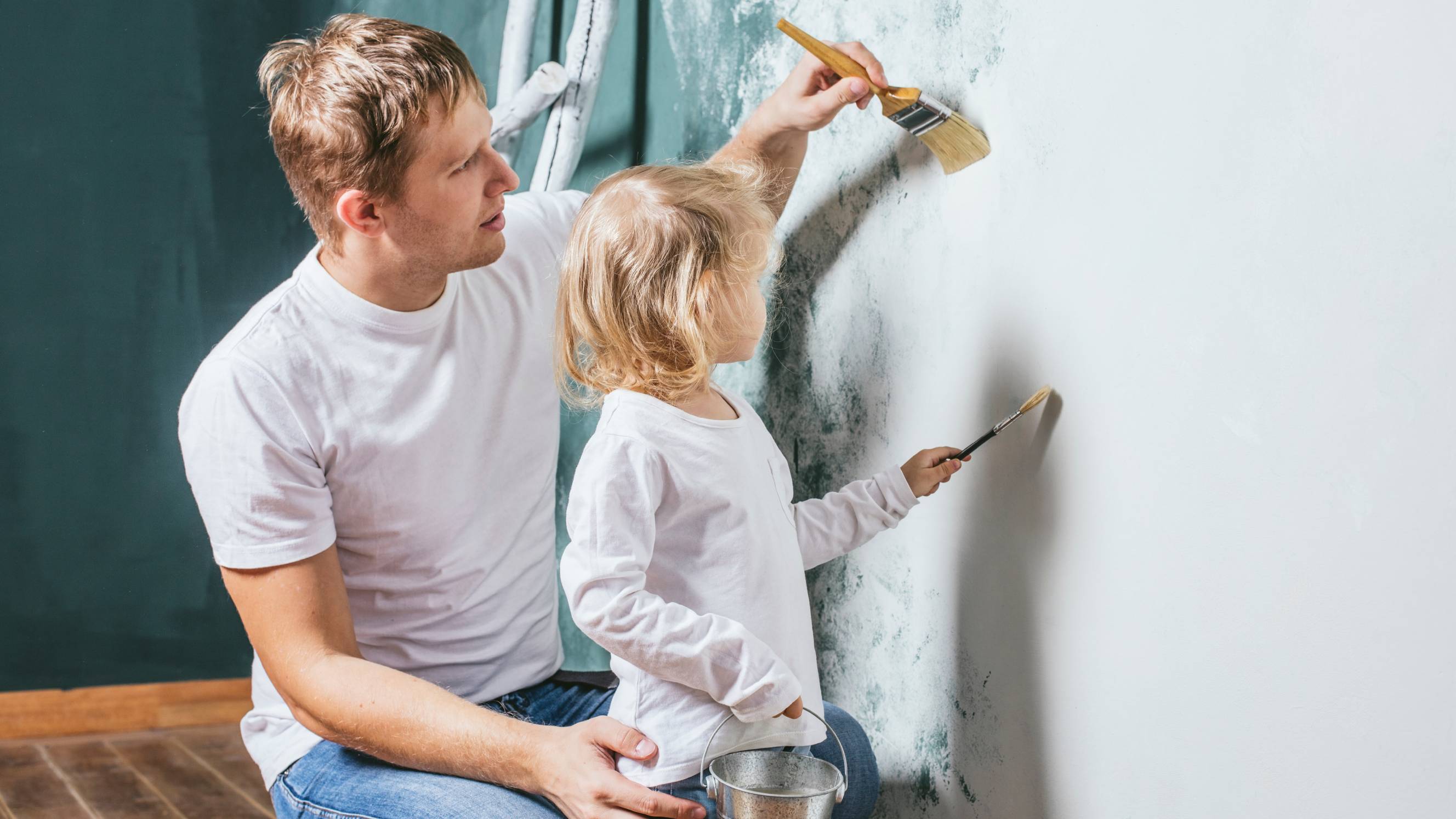 a man and his kid painting an interior wall white