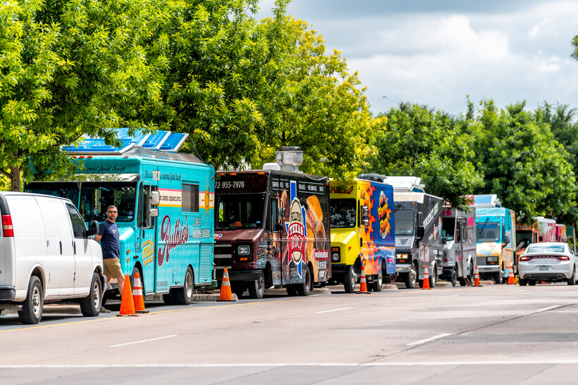 Several colorful food trucks parked along a street next to Klyde Warren Park. - moving to Dallas