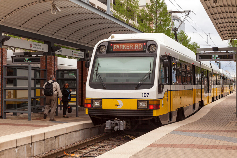 A yellow DART light rail train stopped at a station in the city of Dallas. - moving to Dallas