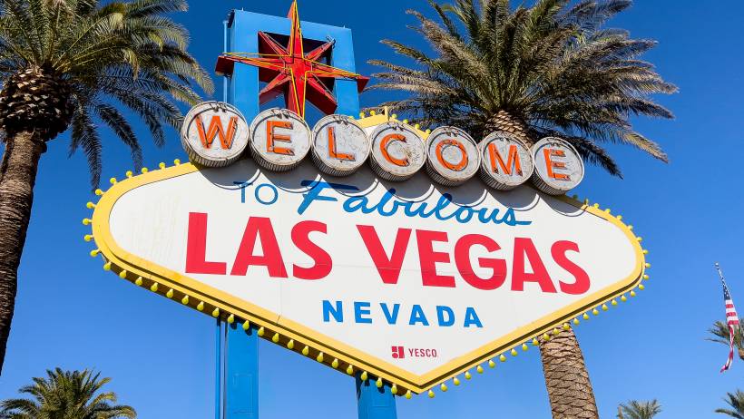 Close-up of the iconic diamond-shaped Welcome to Fabulous Las Vegas sign featuring its classic neon bulbs, red lettering, and starburst topper. - moving to las vegas