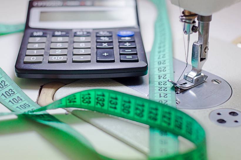 how much does tailoring cost - Calculator with measuring tape beside a sewing machine