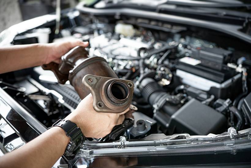 catalytic converter replacement cost - Removed catalytic converter positioned above a car engine compartment