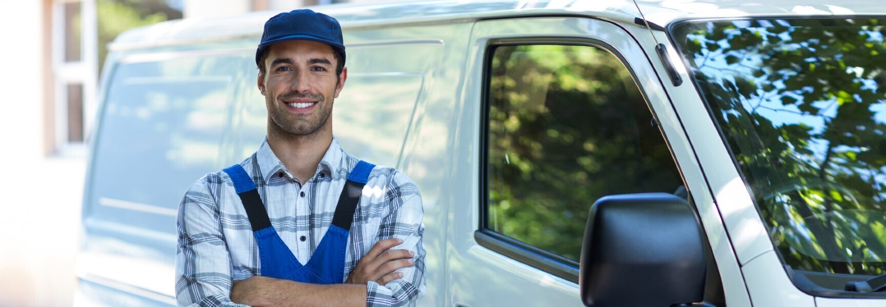 A handyman standing with his arms crossed in front of a white van.